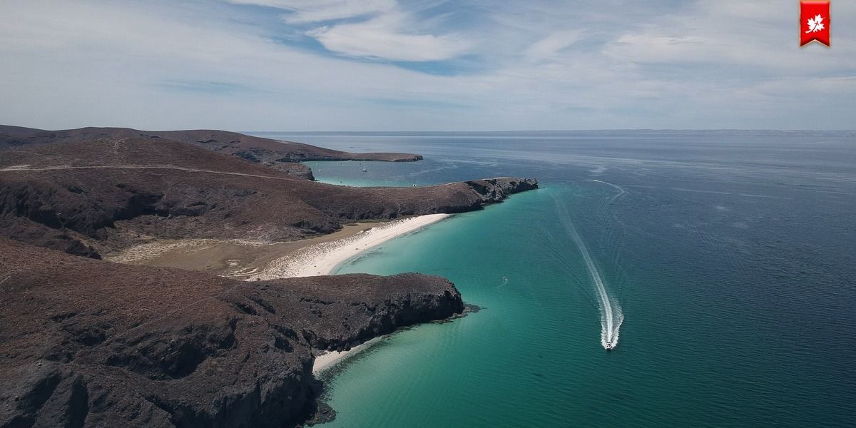 Turquoise bay with a boat wake and white-sand cove, from above – airport transfer to Chileno Bay
