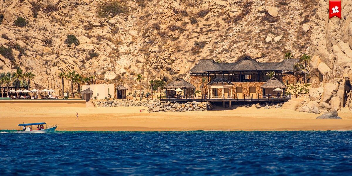 Wooden beachfront building on golden sand below rocky cliffs – airport transfer to Le Blanc