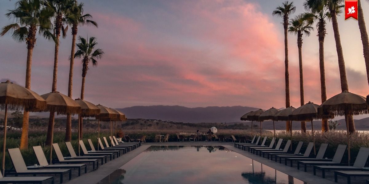 Resort pool with palm trees and umbrellas under a pink sunset sky – airport transfer to Pueblo Bonito