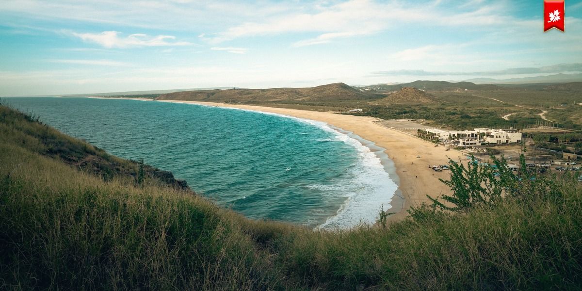 Turquoise waves and a sandy beach seen from a grassy hilltop – airport transfer to Hotel San Cristóbal